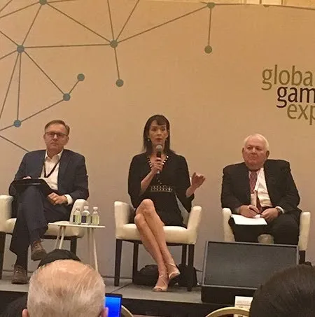 Three professionals seated on stage, one woman speaking into microphone at conference panel.