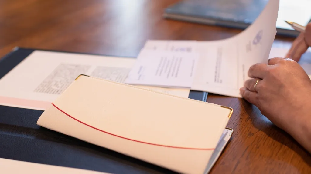Close-up of hands reviewing documents on a wooden table with a white folder and paperwork.
